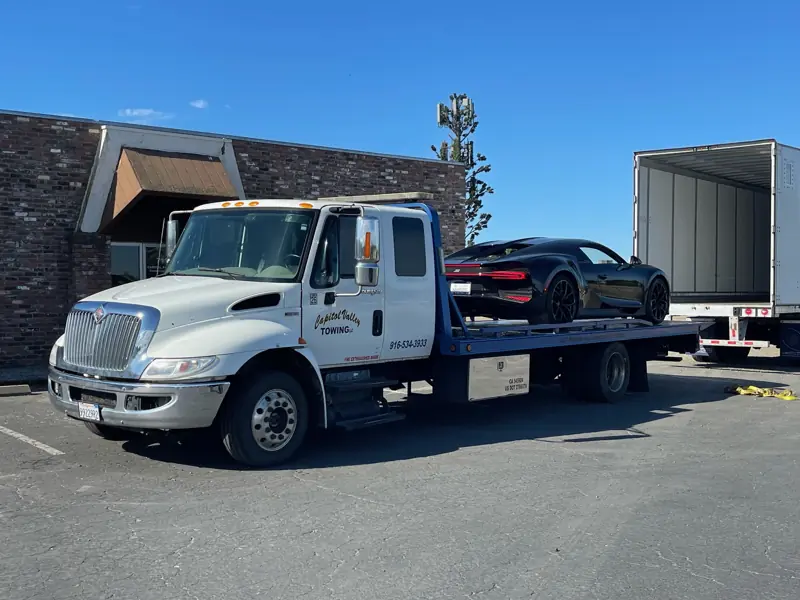 Flatbed carrying a Bugatti next to a box truck