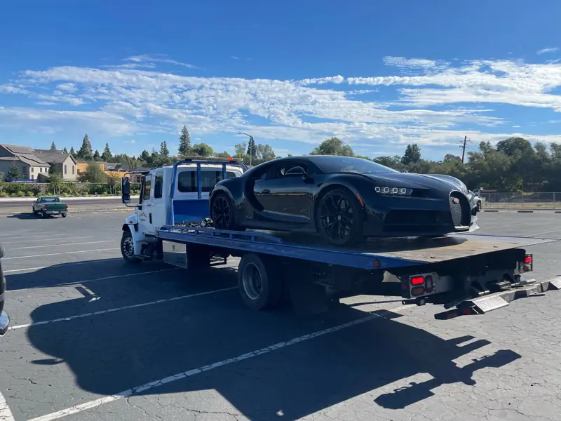 Black Bugatti on a flatbed in a parking lot
