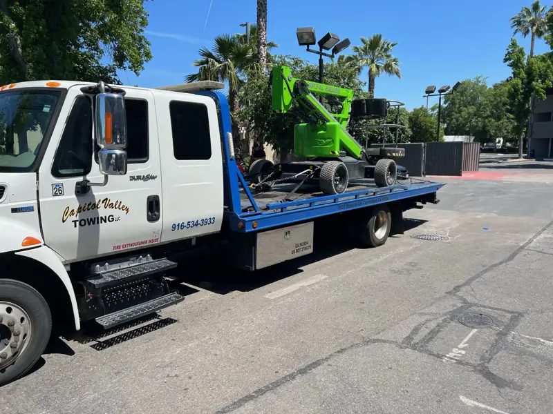 Green construction lift on a flatbed tow truck